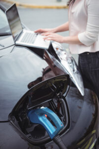 mid section woman using laptop while charging electric car